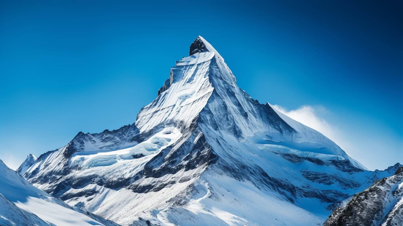 A majestic, snow-capped, pyramid-shaped peak under a clear, deep blue sky.
