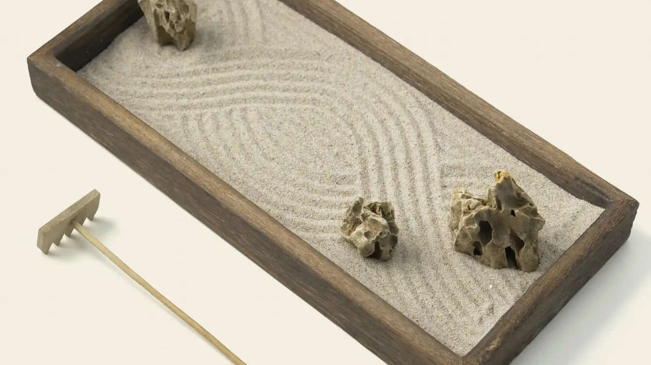 Parallel lines raked through white sand around natural stones in a Zenify karesansui garden