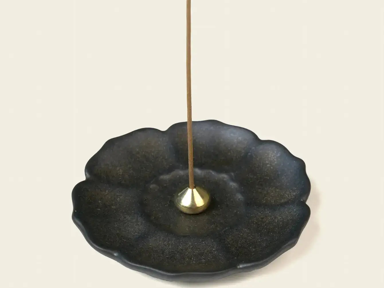 Dark ceramic lotus-shaped incense tray with a small brass holder and an unlit incense stick.