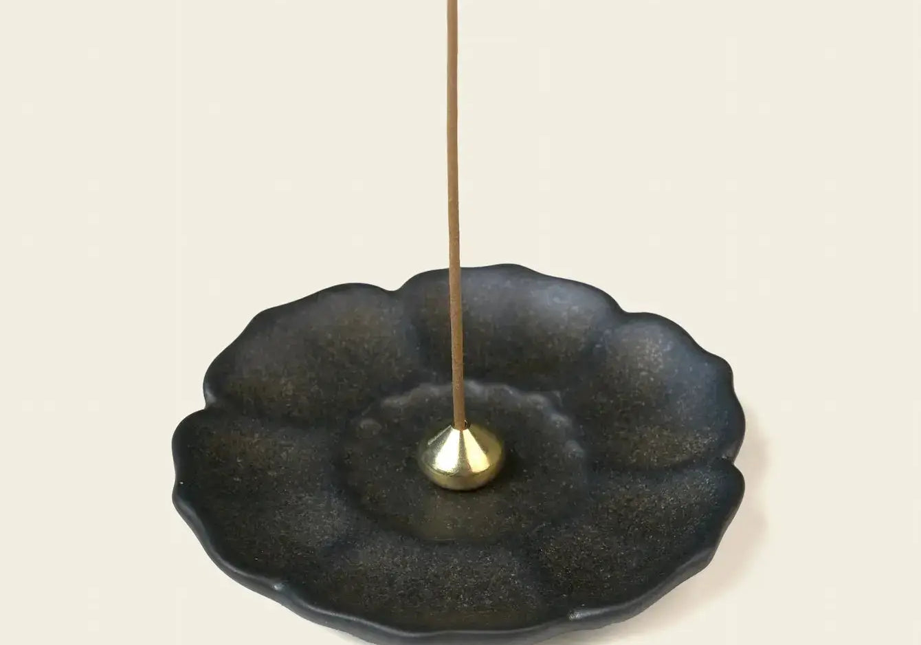 Dark ceramic lotus-shaped incense tray with a small brass holder and an unlit incense stick.