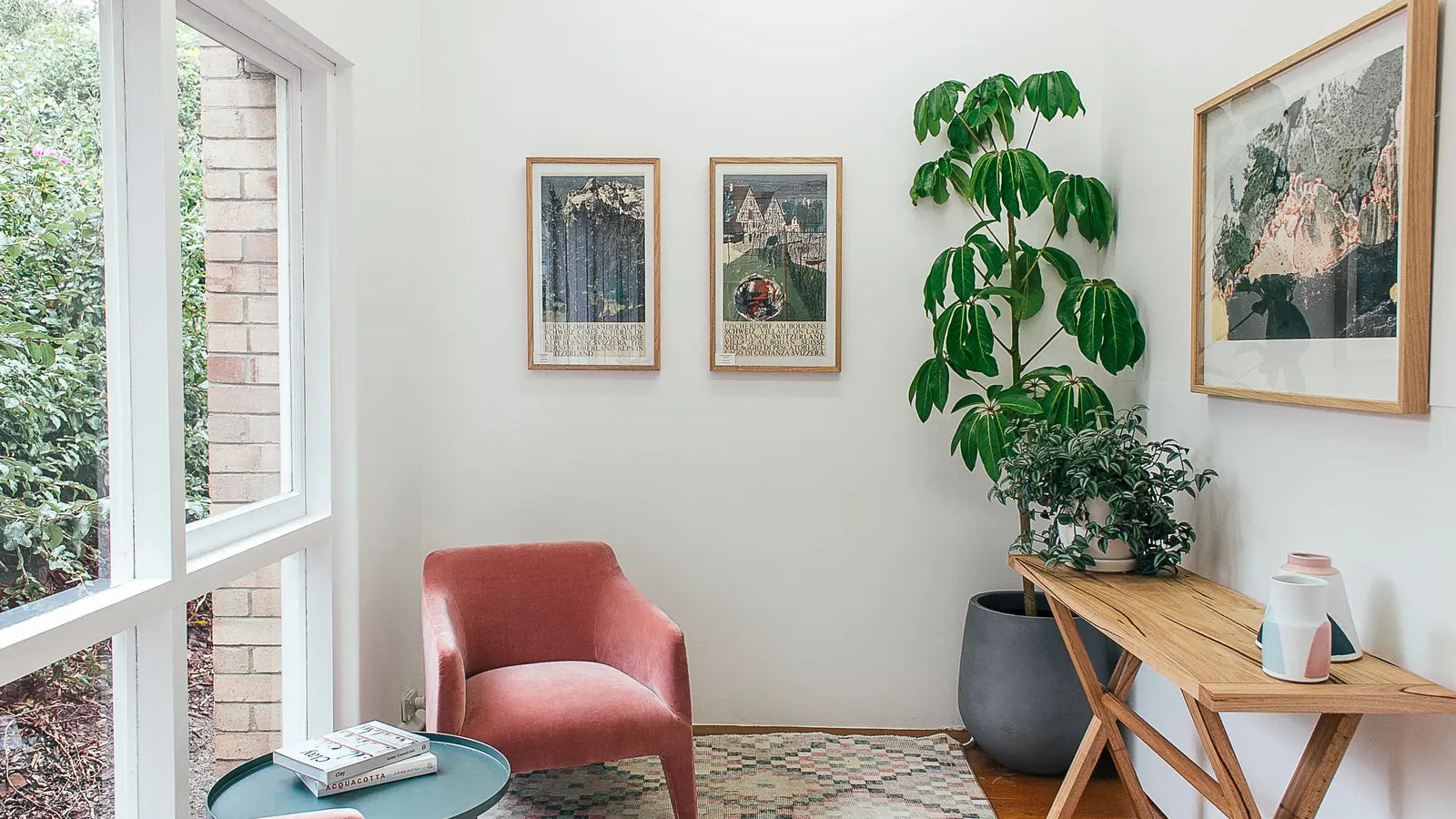 A pink armchair beside large windows, indoor plants, and a wooden console table.