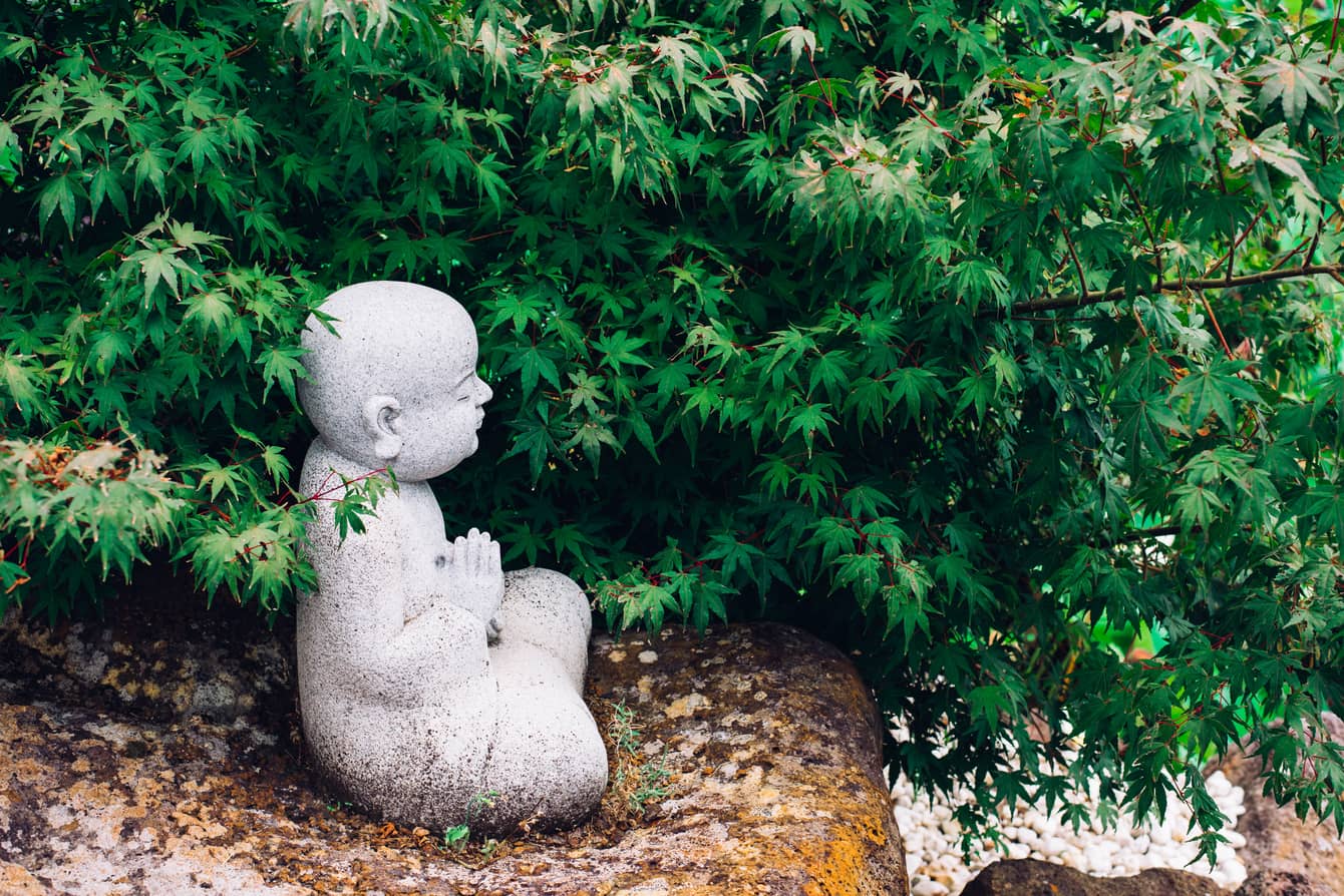 Statue of a child meditating among greenery, representing the essence of What Is Zen.
