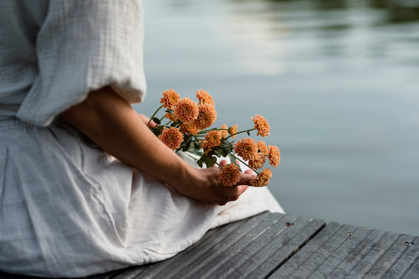 A woman in a white dress holding a bouquet of orange flowers by a calm lake, reflecting the truth about energy.