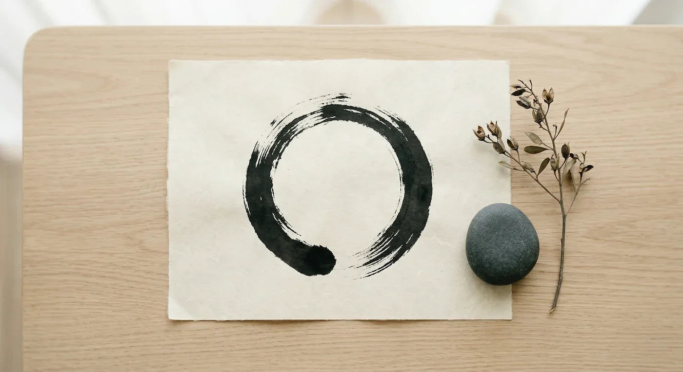 The Beginner's Guide to Zen symbol drawn on paper with a stone and a branch on a wooden table.
