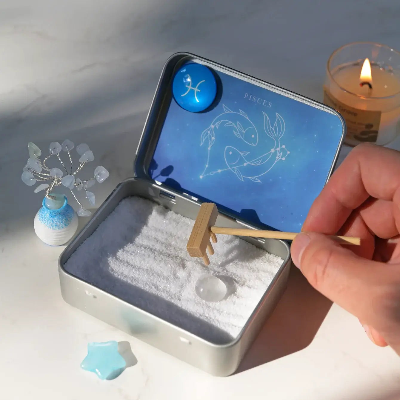 Person arranging the Pisces Crystal Zen Garden with aquamarine tree, blue aventurine star, and white sand.