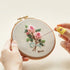 Close-up of hands stitching a floral design in the 5-Hour Mindfulness Embroidery Kit with a wood stand.