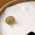 Zen Garden featuring a smooth, greenish stone resting on white sand with gentle patterns for tranquility and relaxation.