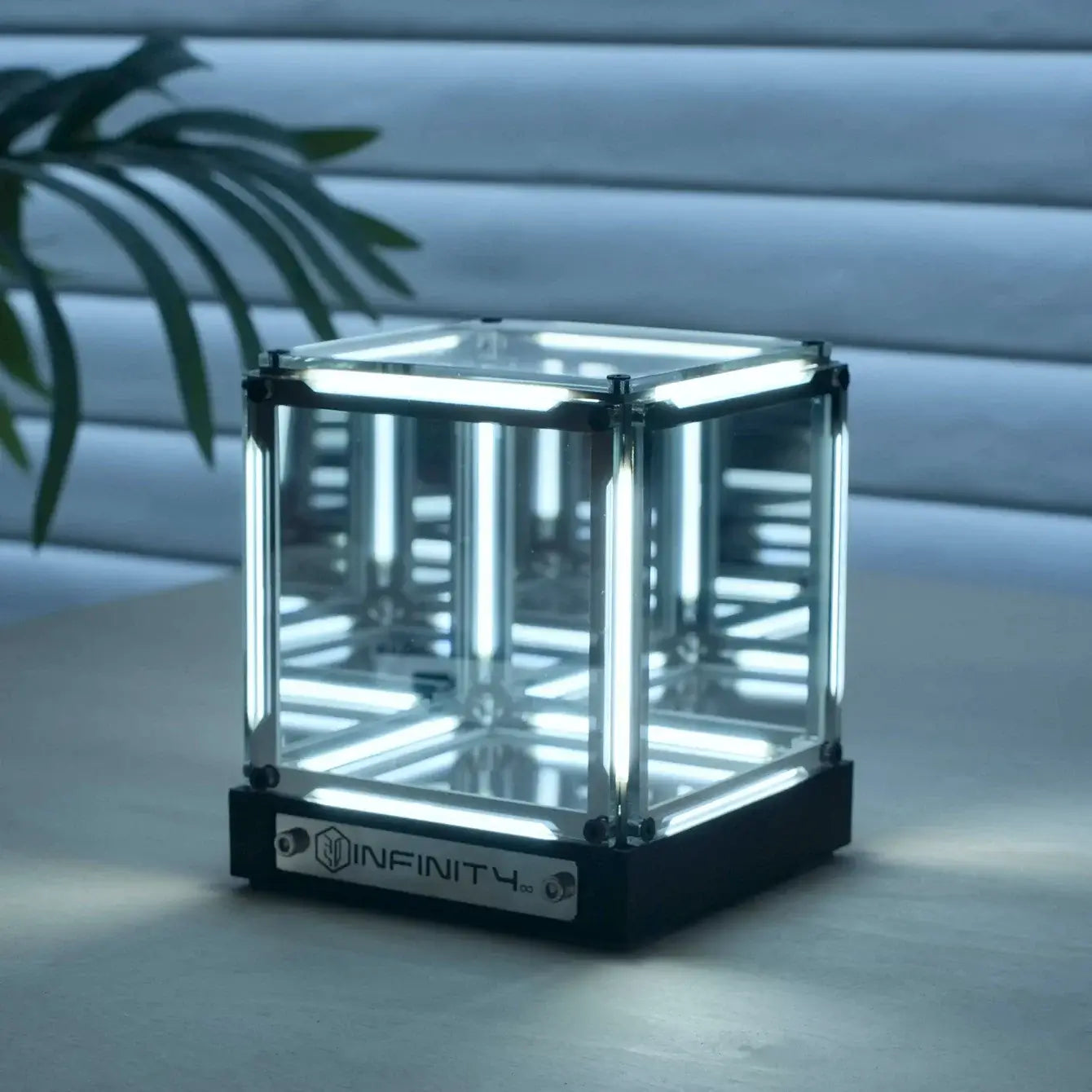 Glass cube with LED lighting on a wooden surface, featuring the 'INFINITY' brand.