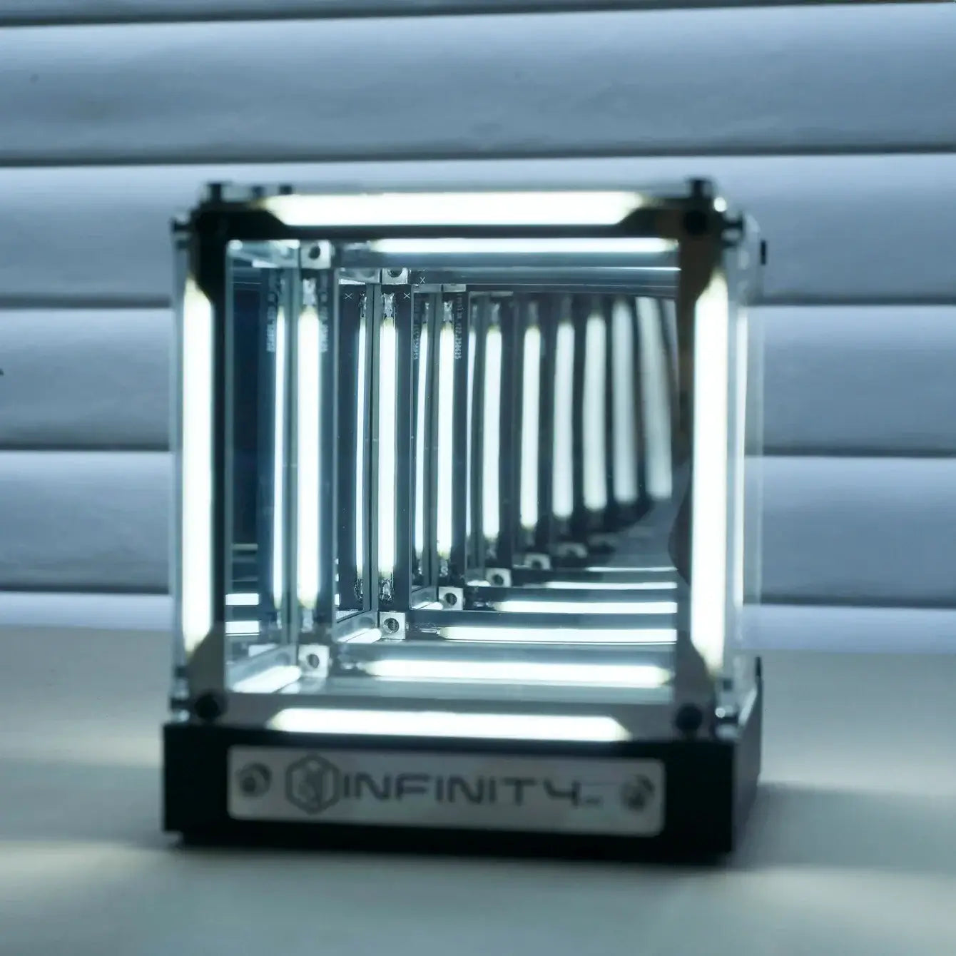 Glass container with metallic frame on a reflective surface, featuring the 'INFINITY' brand.