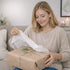 Woman joyfully unwrapping a beautifully wrapped gift with a smile in a cozy living room setting.