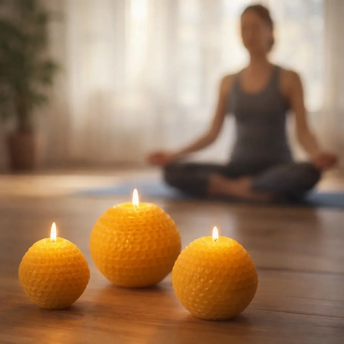 Three glowing Beeswax Candles in geometric forms with a person meditating in the background, creating a calming atmosphere.