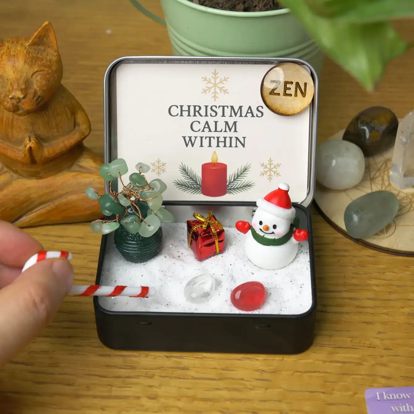 Zenify™ Christmas Zen Pocket Garden — a festive mini Zen set with a green aventurine tree, snowman, gift box, candy cane, and healing crystals on white sand.