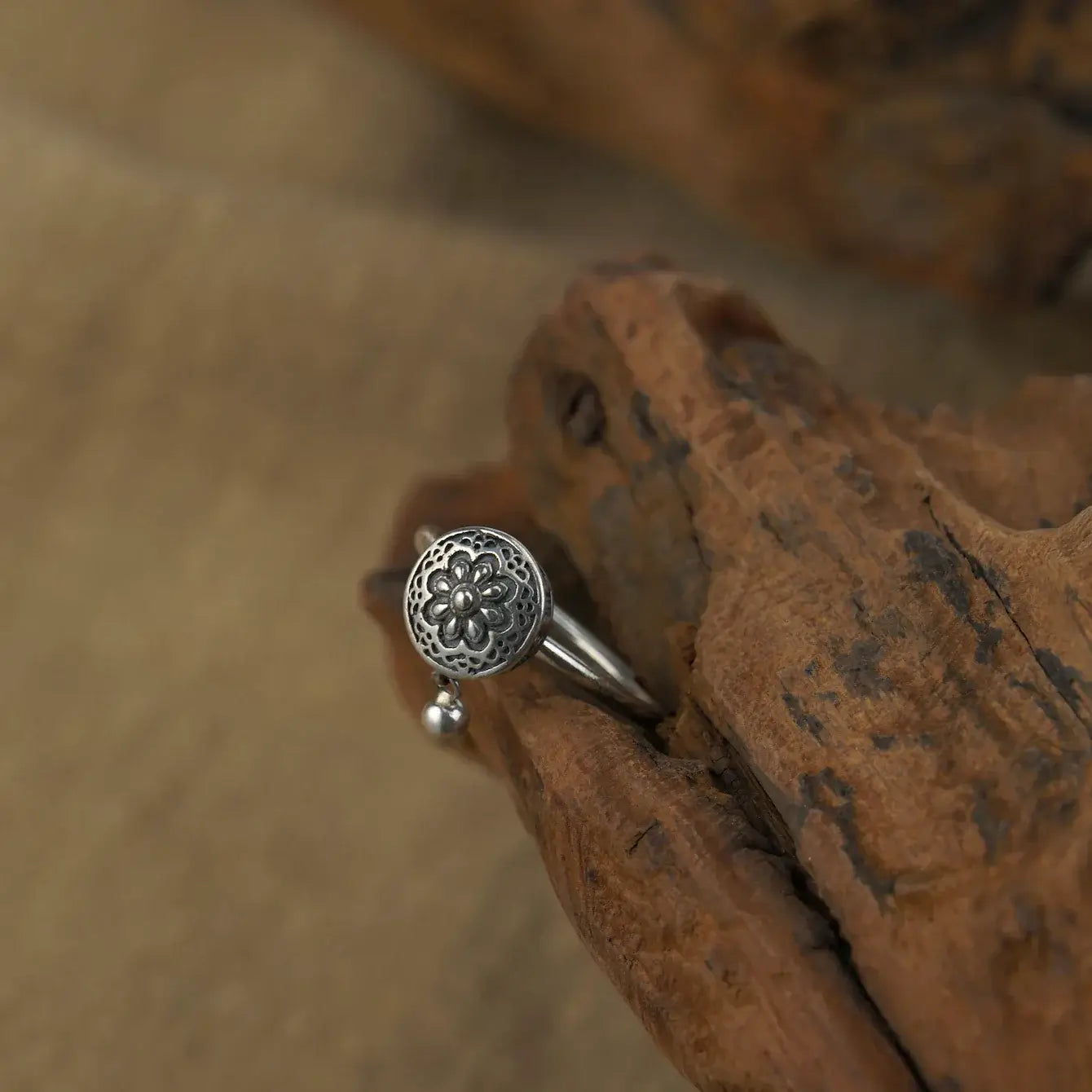 Zenify™ Silver Mantra Ring on wooden surface showcasing unique floral design and sterling silver craftsmanship.