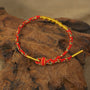 Zenify™ Fortune Knot - Handwoven Lucky Cord Bracelet in red and gold resting on wood background.