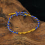 Zenify™ Fortune Knot – Handwoven lucky cord bracelet in blue and gold on wooden background.