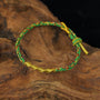 Zenify™ Fortune Knot – Handwoven Lucky Cord Bracelet in green and gold resting on wood.