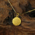 Close-up of Zenify™ Dual Blessings gold plated pendant featuring intricate designs on a wooden background.