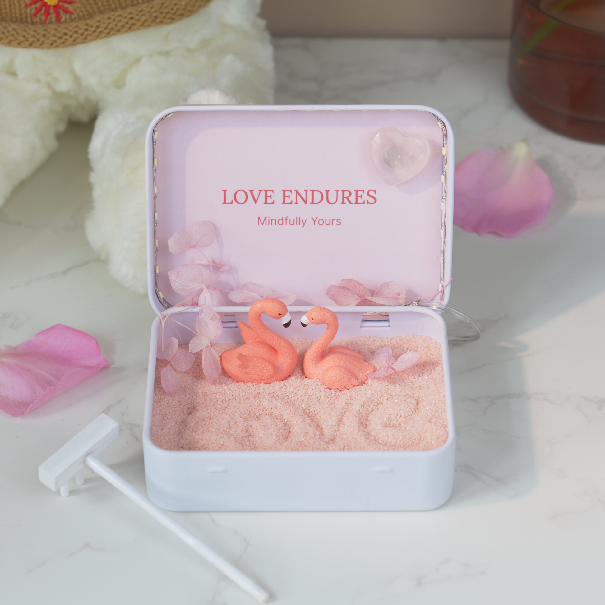 Love Endures Crystal Zen Garden with pink sand and flamingo figurines in a decorative box on a table.