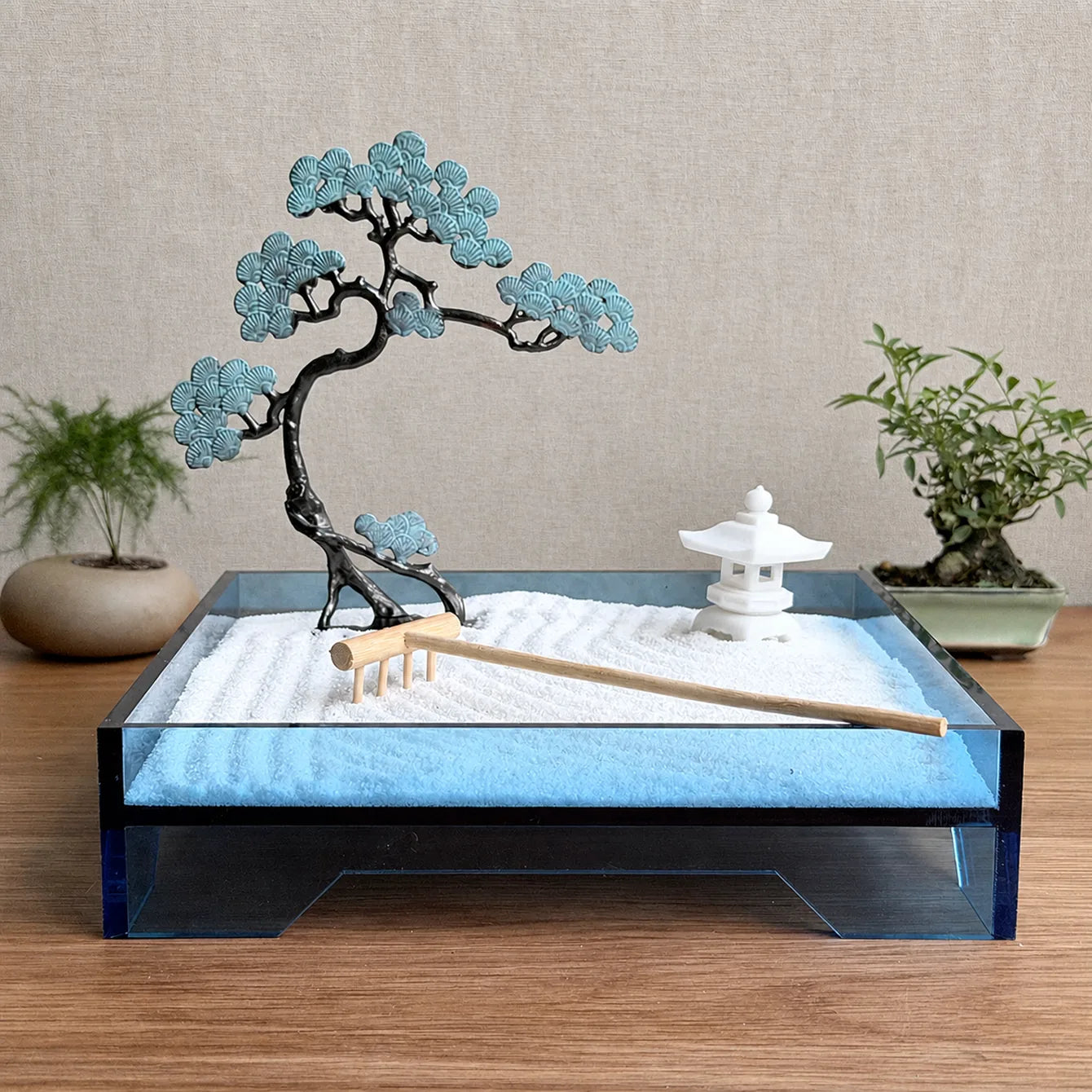 Blue acrylic Zen garden displayed on a wooden desk with copper pine tree, white sand and wooden rake