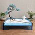 Blue acrylic Zen garden displayed on a wooden desk with copper pine tree, white sand and wooden rake