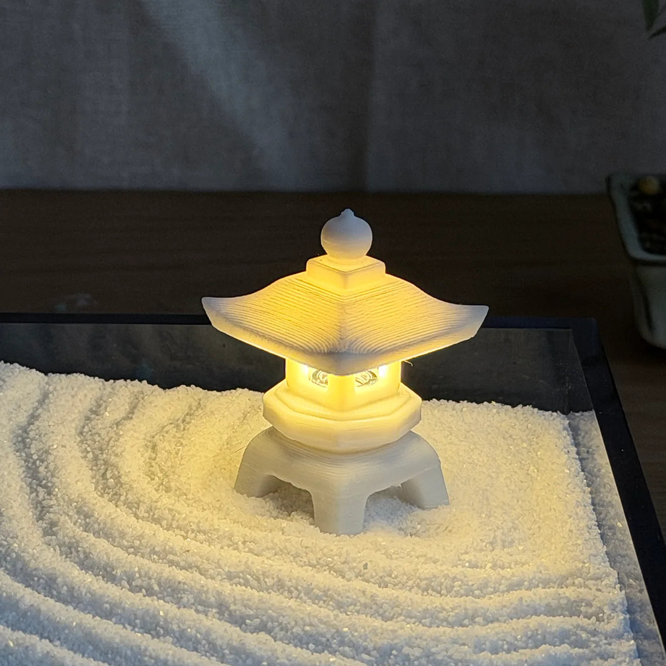 Close-up of the battery-powered resin stone lantern glowing over raked fine white sand