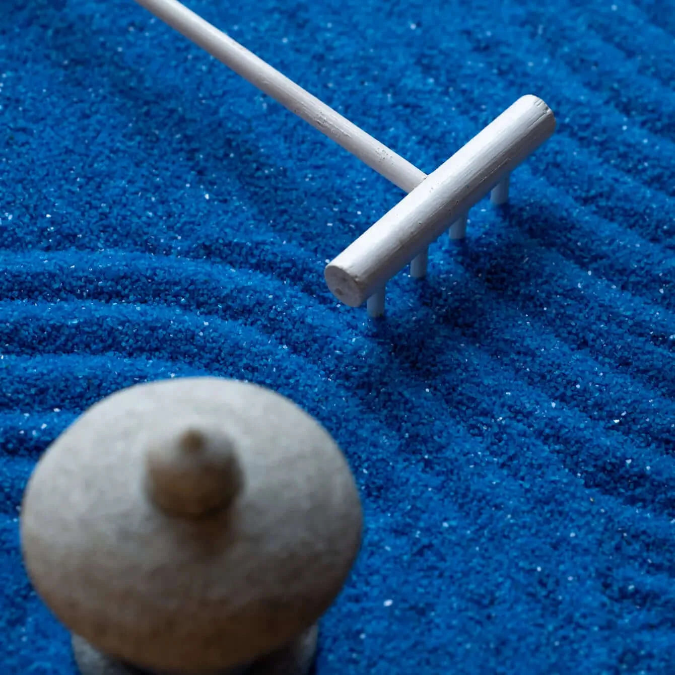 Close-up of deep blue raked sand, white rake, and miniature stone lantern in the Blue Zen Garden.
