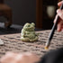 Small green glazed ceramic meditation frog on calligraphy paper beside a brush.