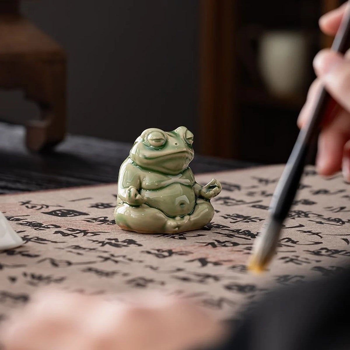 Small green glazed ceramic meditation frog on calligraphy paper beside a brush.