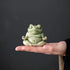 Small green glazed ceramic meditation frog resting on one palm to show its scale.