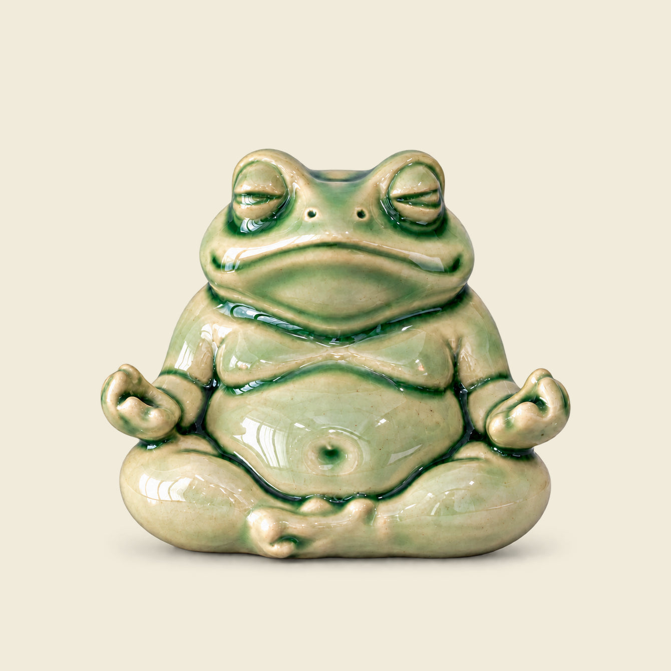 Small celadon green glazed ceramic frog seated in meditation on a warm ivory background.