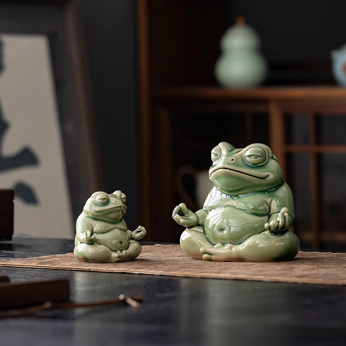 Small and large green glazed ceramic meditation frogs displayed together on a brown cloth; sold individually.