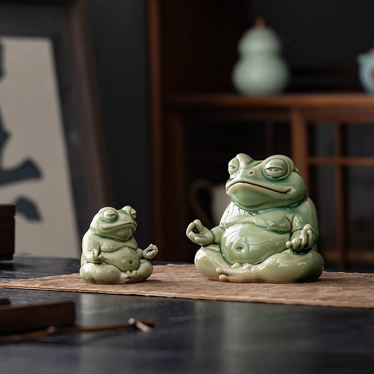 Small and large green glazed ceramic meditation frogs displayed together on a brown cloth; sold individually.