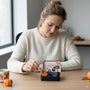 Woman opening a Halloween-themed tea box at a table with pumpkins and a cup.