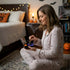 Woman in pajamas sitting on a bed in a Halloween-themed room.