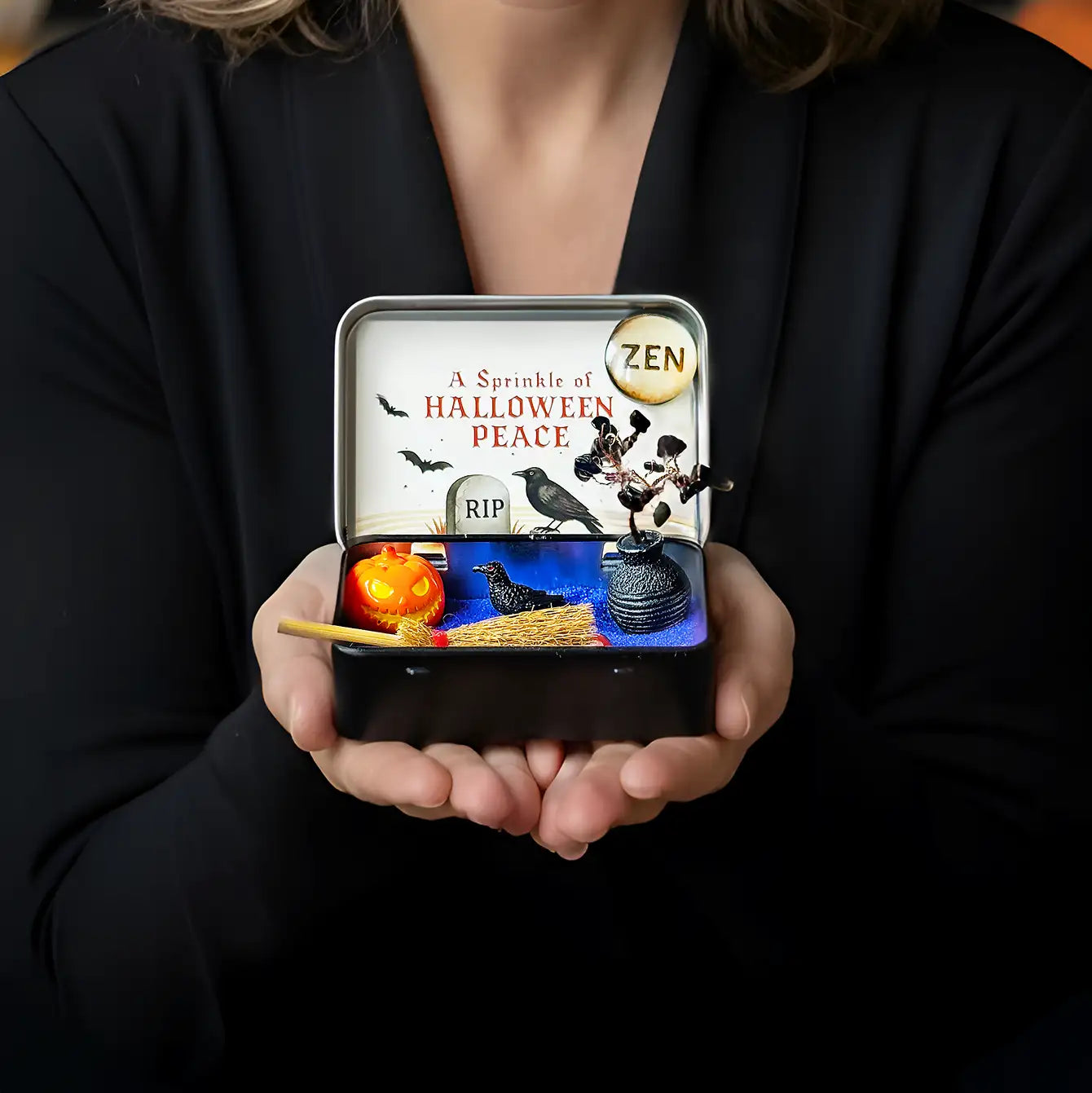 Person holding a small Halloween-themed tin with various elements.