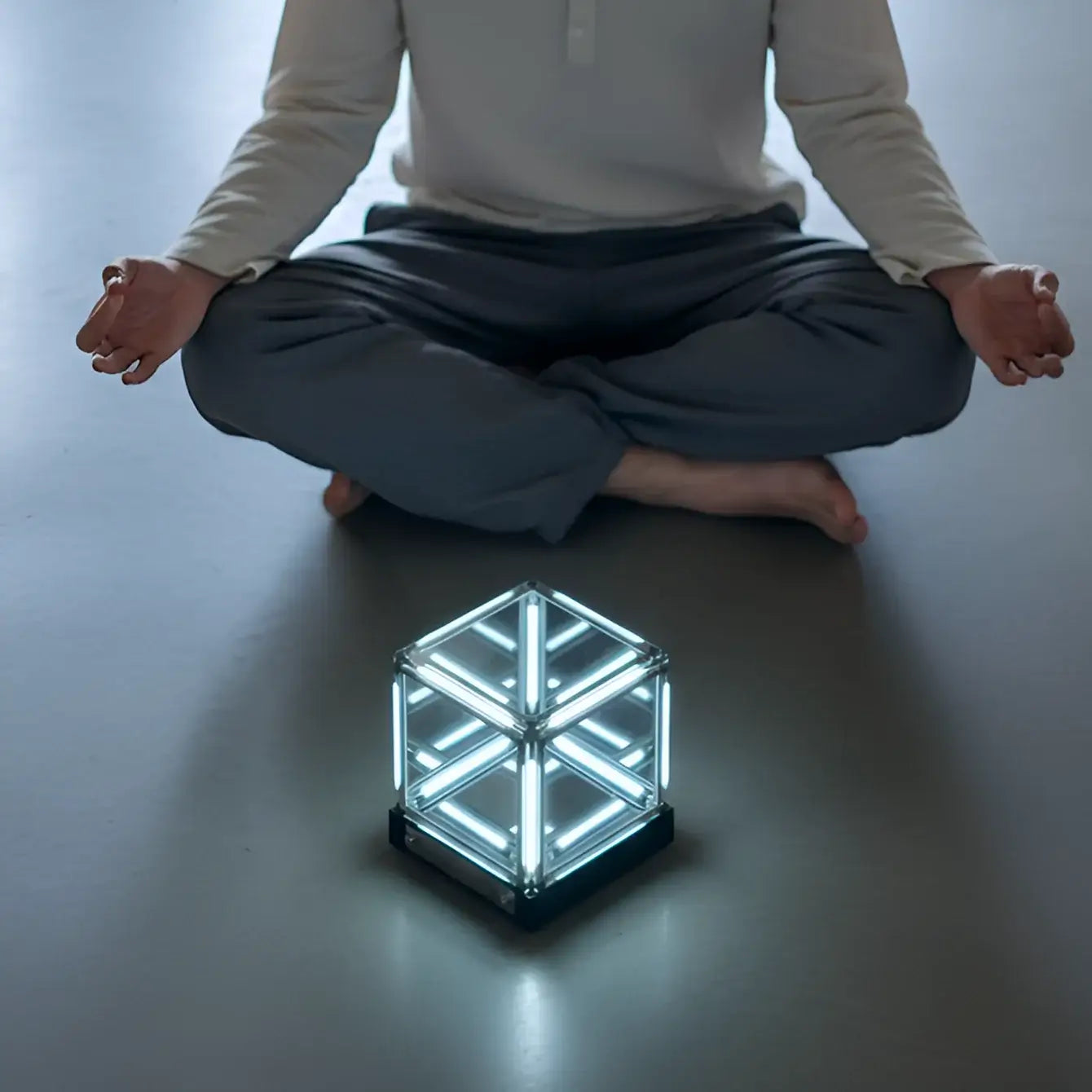 Person meditating with a glowing cube on the floor