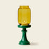 Yellow glass candle holder on a green base against a beige background