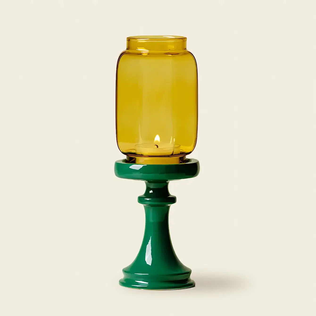 Yellow glass candle holder on a green base against a beige background