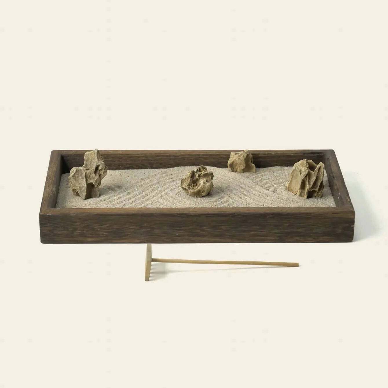 Japanese Karesansui Zen Garden with three natural stones arranged in raked white sand and a wooden rake.
