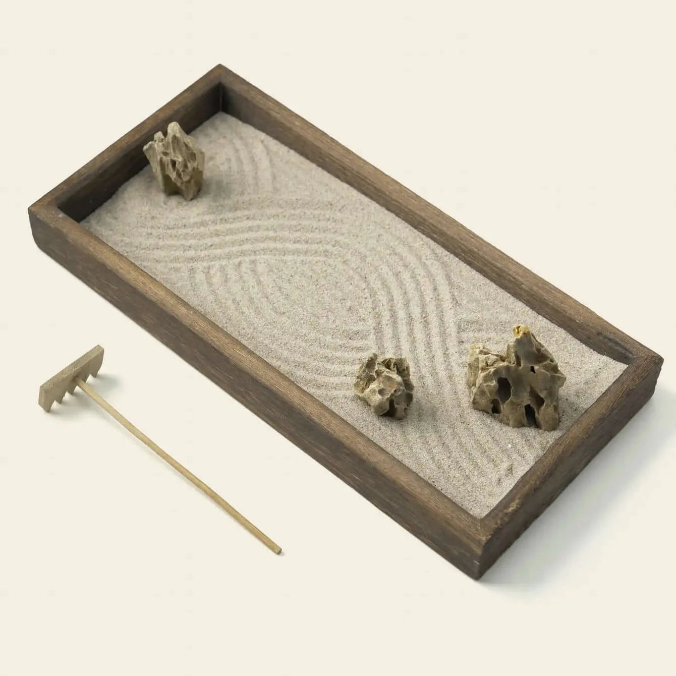 Angled close-up of the Japanese Karesansui Zen Garden with natural stones, raked white sand, dark wood tray, and wooden rake.
