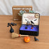 Classic Halloween Zen Garden on a wooden desk with purple sand, obsidian tree, pumpkin, raven and miniature broom arranged beside the tin.