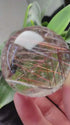 Zenify™ Rutilated Quartz Crystal Sphere showcasing golden rutile threads in a hand for energy flow and clarity.