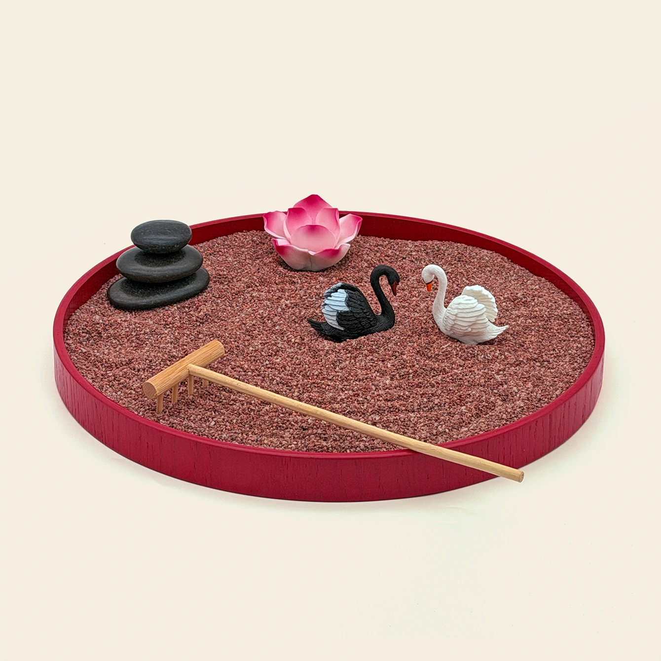 Red oval Zen garden with red sand, stacked stones, lotus, black and white swans, and bamboo rake