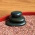 Close-up of three stacked black stones in red Zen garden sand