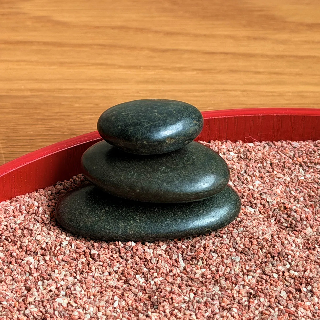 Close-up of three stacked black stones in red Zen garden sand