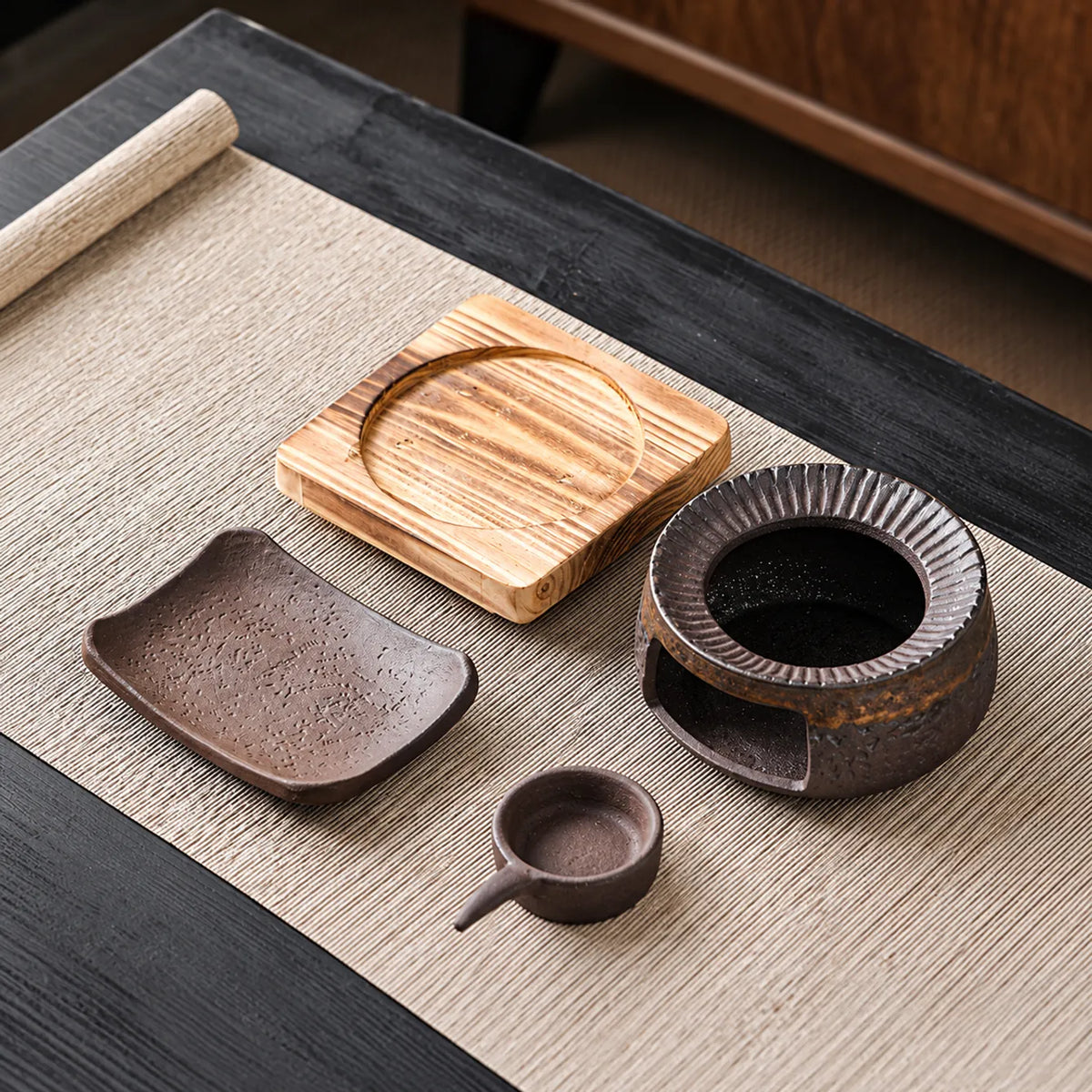 Wooden base, round ceramic warmer body, curved dish, and handled candle cup arranged separately on a woven mat.