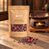 Nightfall 20 g kraft pouch with lavender and rose petals on a stone surface, with a softly blurred ceramic warmer and small candle flame behind.