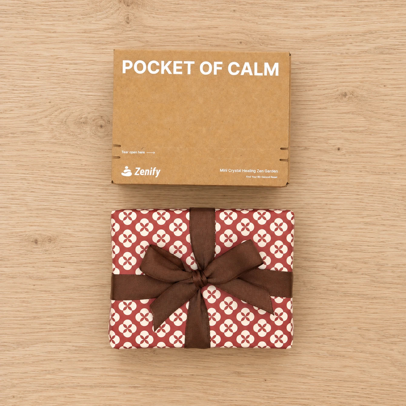 Zenify Pocket of Calm kraft box above a red-and-cream gift-wrapped package with a brown ribbon on a light white oak tabletop.