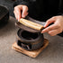 Hands displaying the removable dish above the ceramic warmer and wooden base, with the empty ceramic candle cup visible inside.