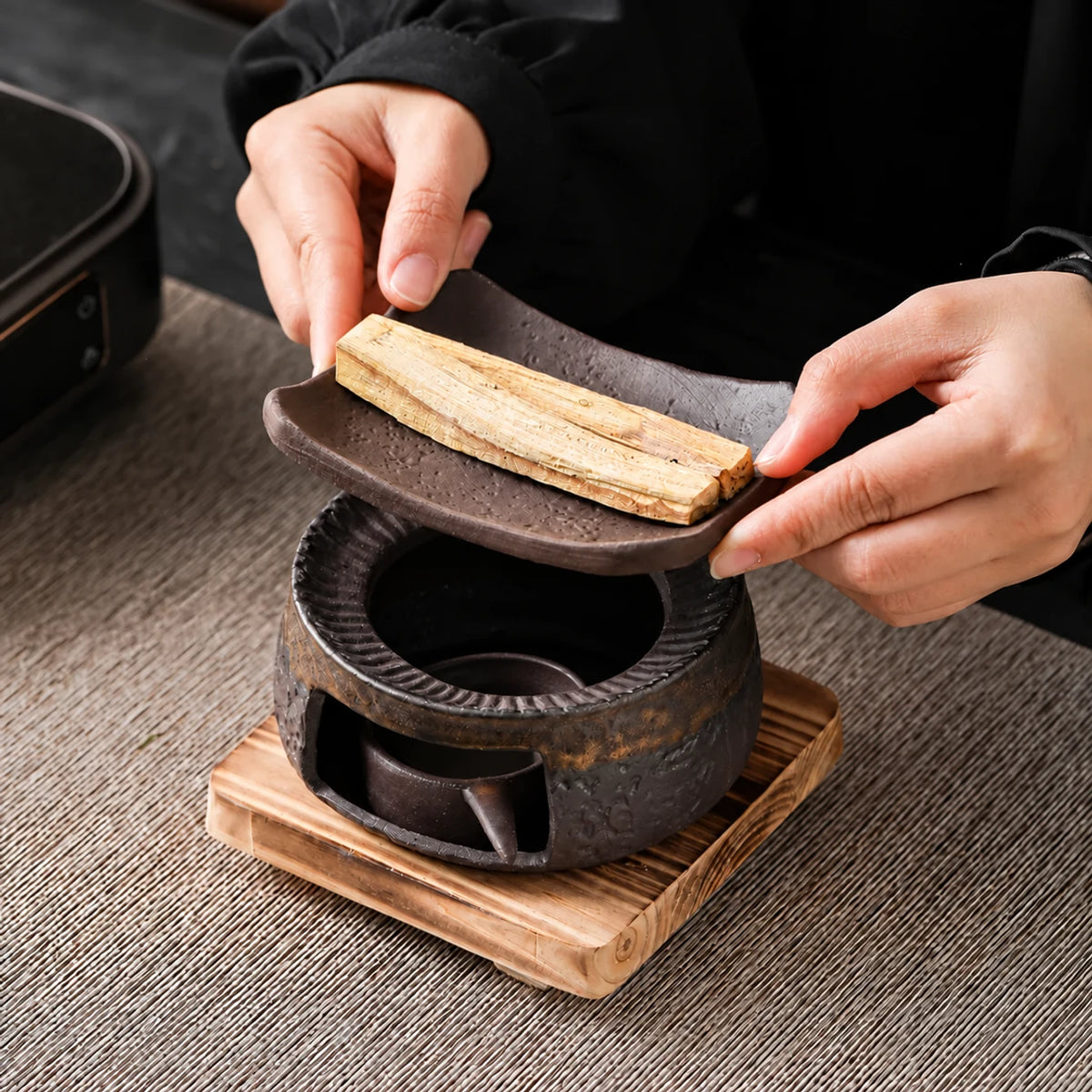 Hands displaying the removable dish above the ceramic warmer and wooden base, with the empty ceramic candle cup visible inside.